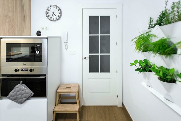 Cocina blanca con horno, microondas, tiestos y puerta al fondo